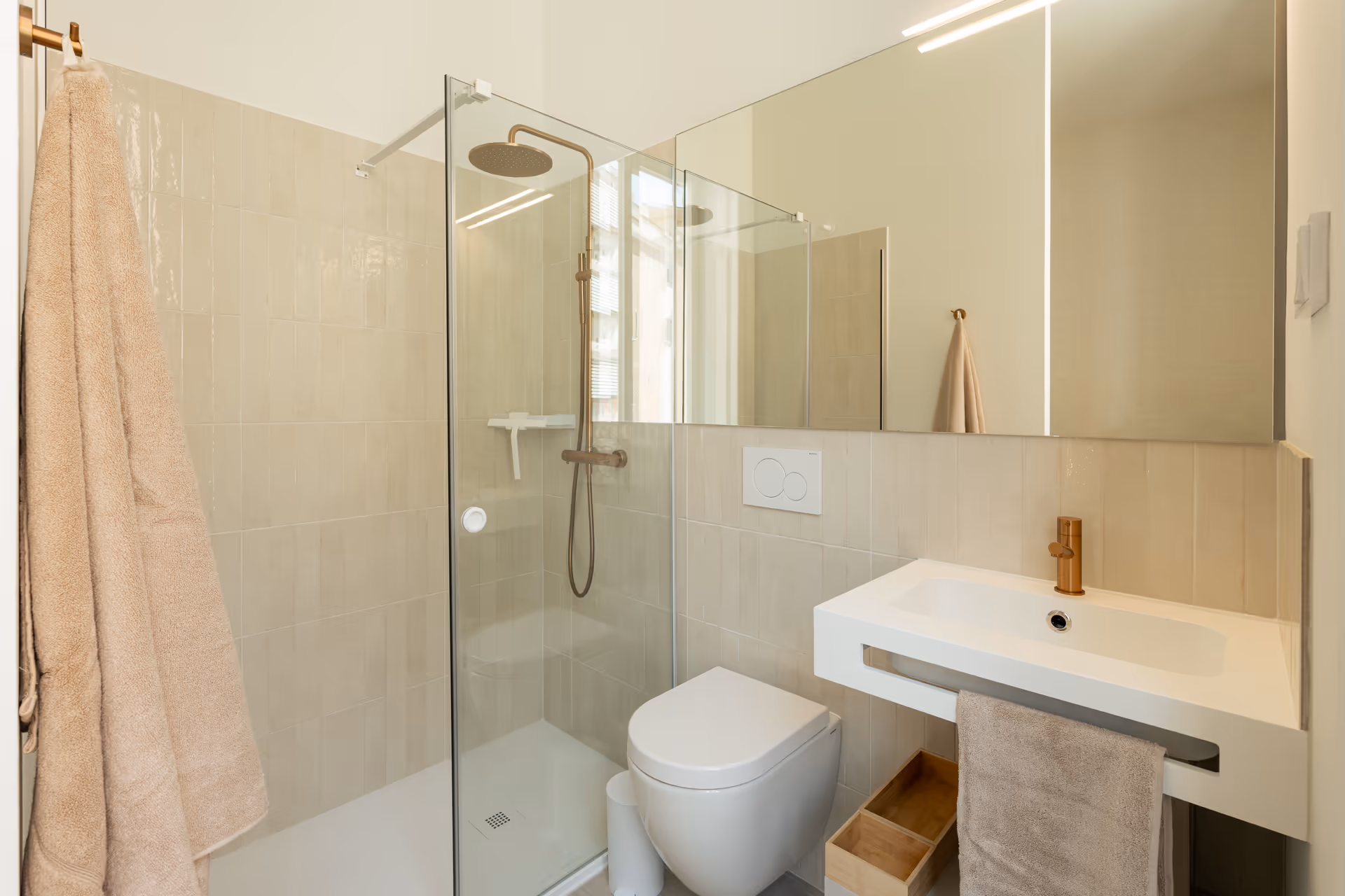 The bathroom in the Azuri residence has a walk-in shower with a bronze rain shower head and a modern white sink with a matching tap.