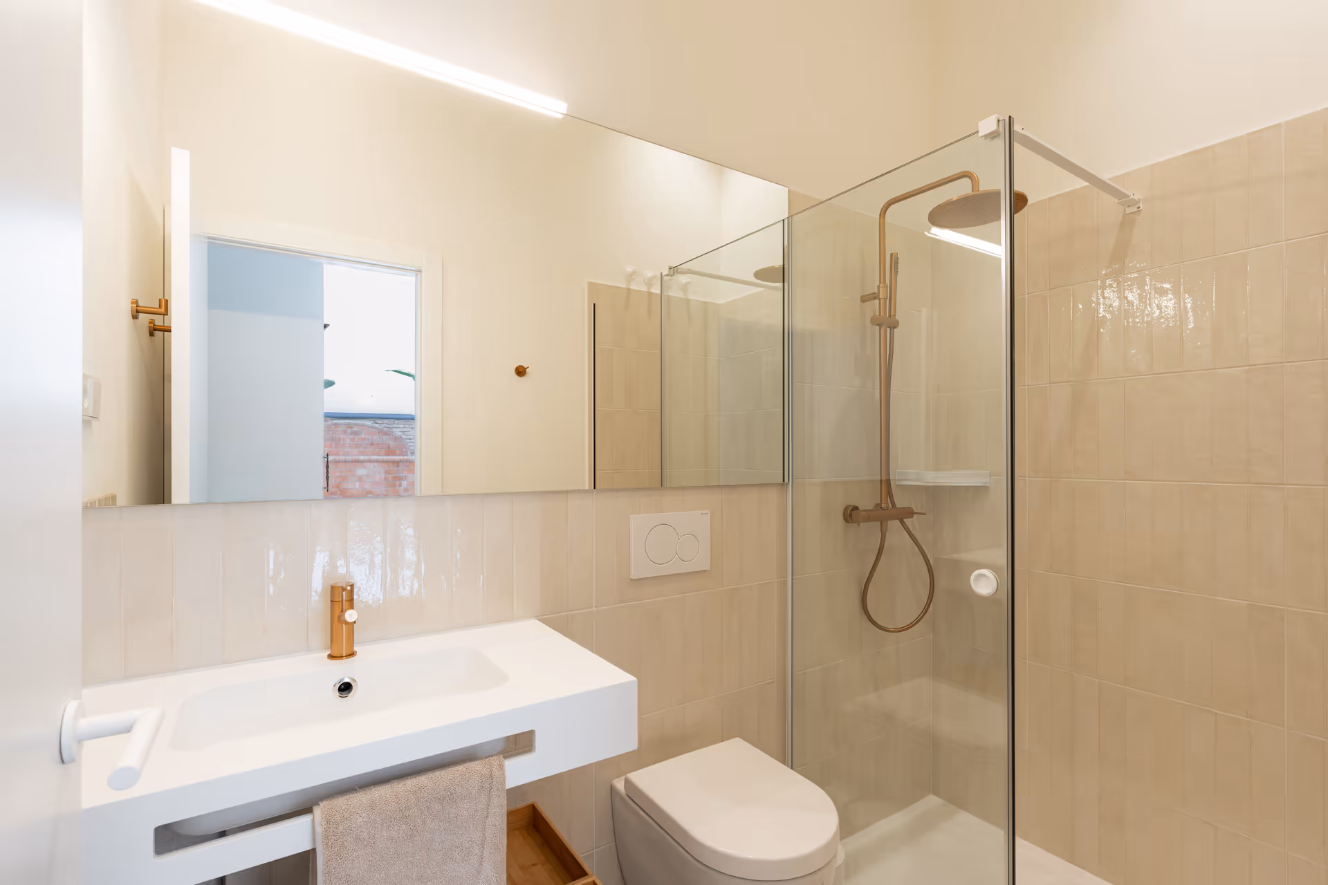 The bathroom in the Oliva residence, with a walk-in shower, floating vanity, and rose gold fittings against glossy beige tiles