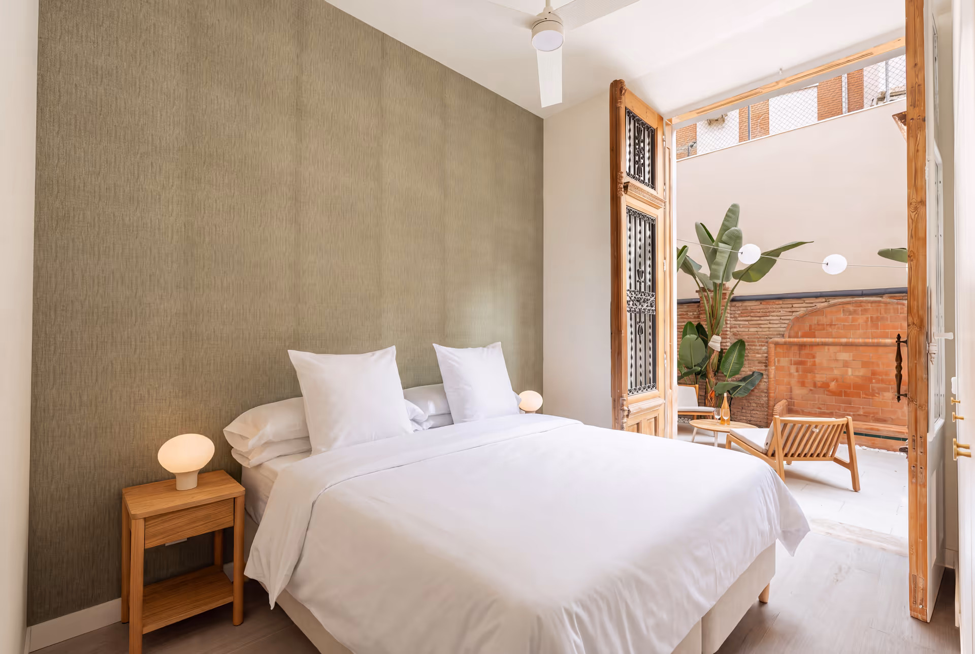 Bedroom in the Oliva residence with a double bed, sage green feature wall, and large antique wooden doors open to a private patio