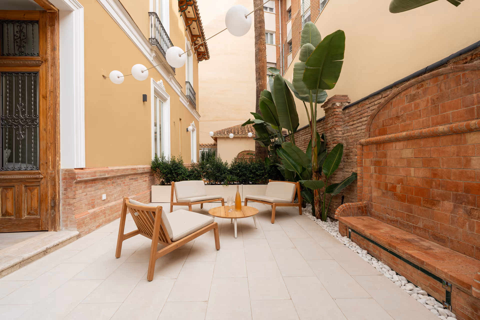 The private terrace of the Oliva residence, with wooden armchairs and a coffee table by a historic brick wall feature