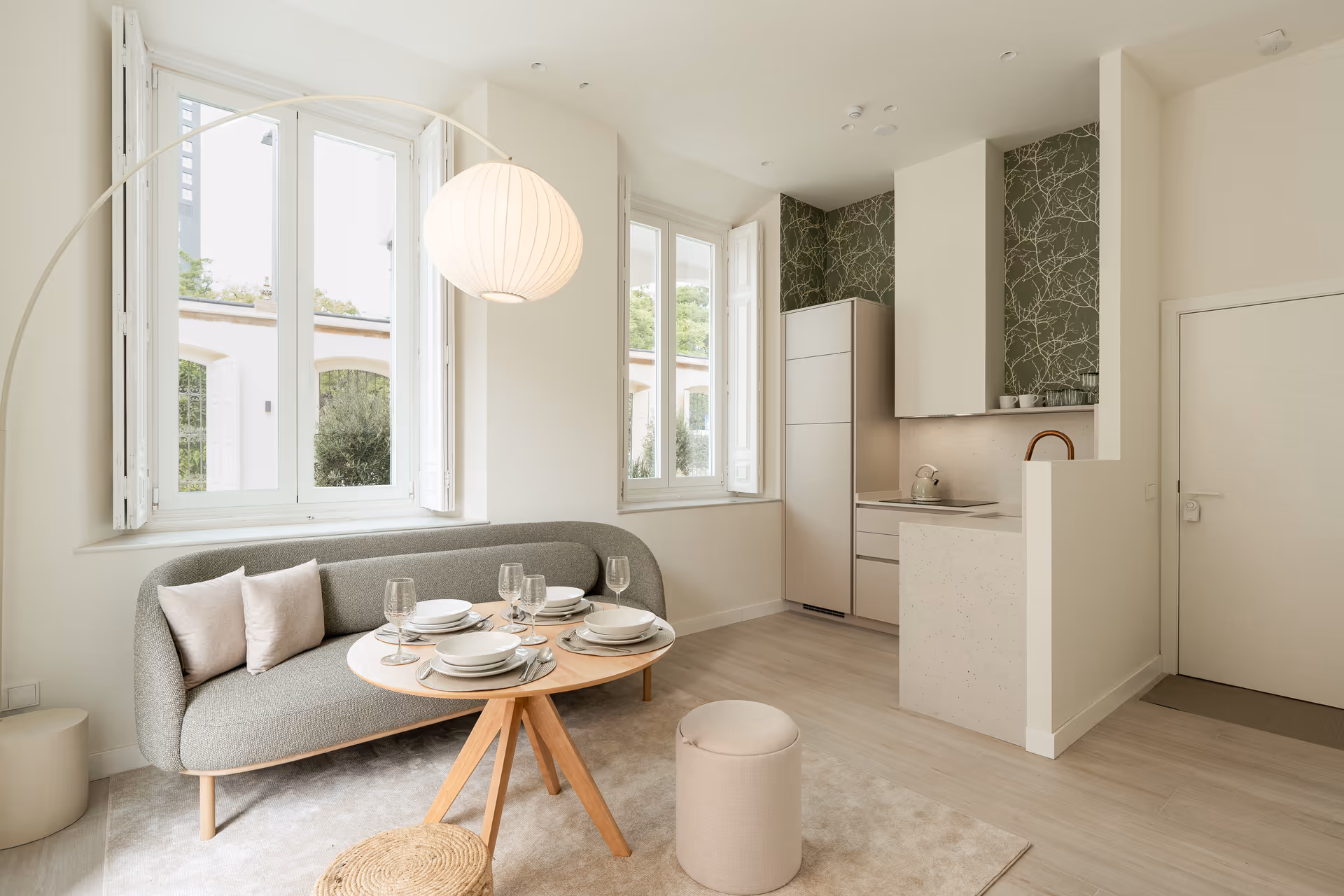 The open-plan living area in the Oliva residence, showing the dining table, curved sofa, and compact kitchen with green wallpaper