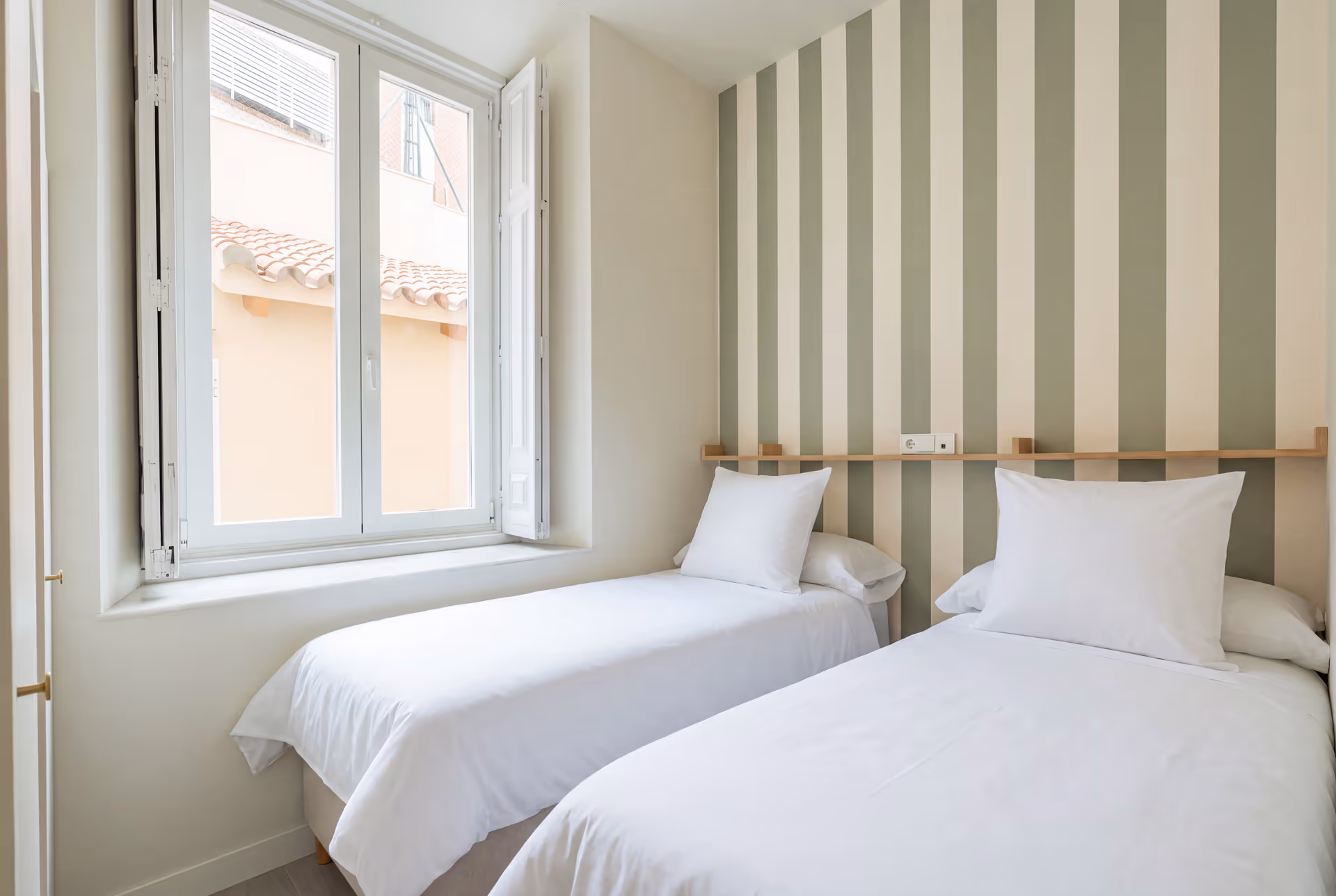 Twin bedroom in the Oliva residence with two single beds, white bedding, and a sage green and white striped feature wall