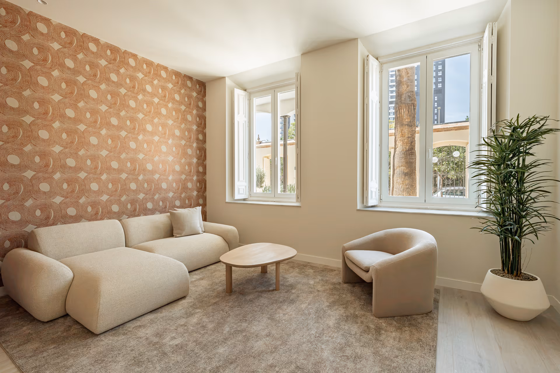 Living room in the Vino residence with a cream bouclé sofa and armchair, and a feature wall with terracotta patterned wallpaper