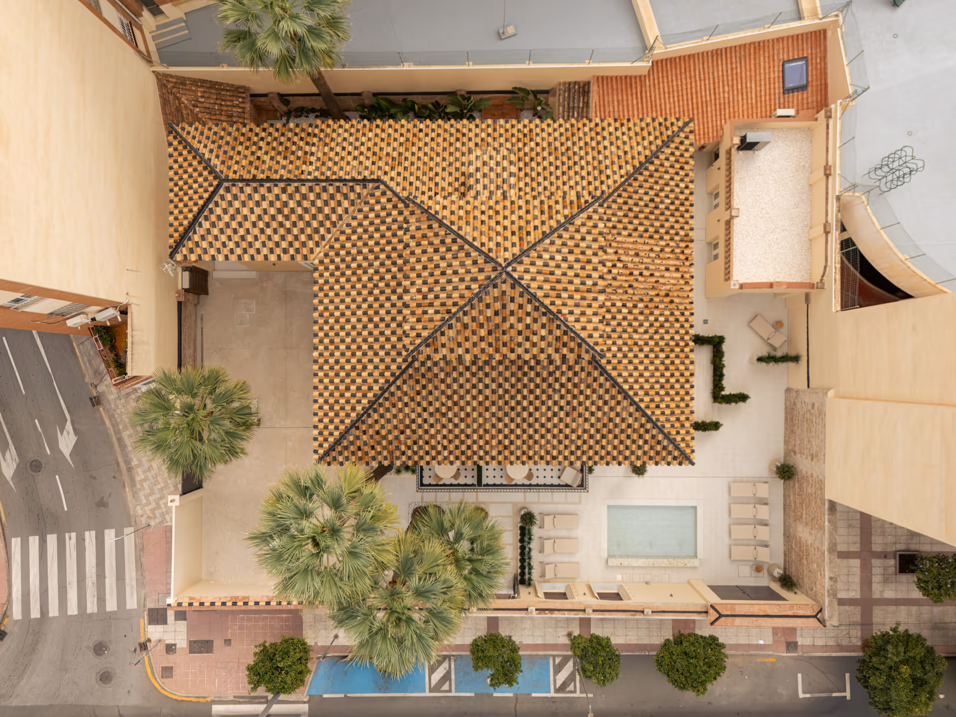 Aerial view of Palacete 10, showing the distinctive chequerboard tiled roof, courtyard with pond, and surrounding Málaga neighbourhood
