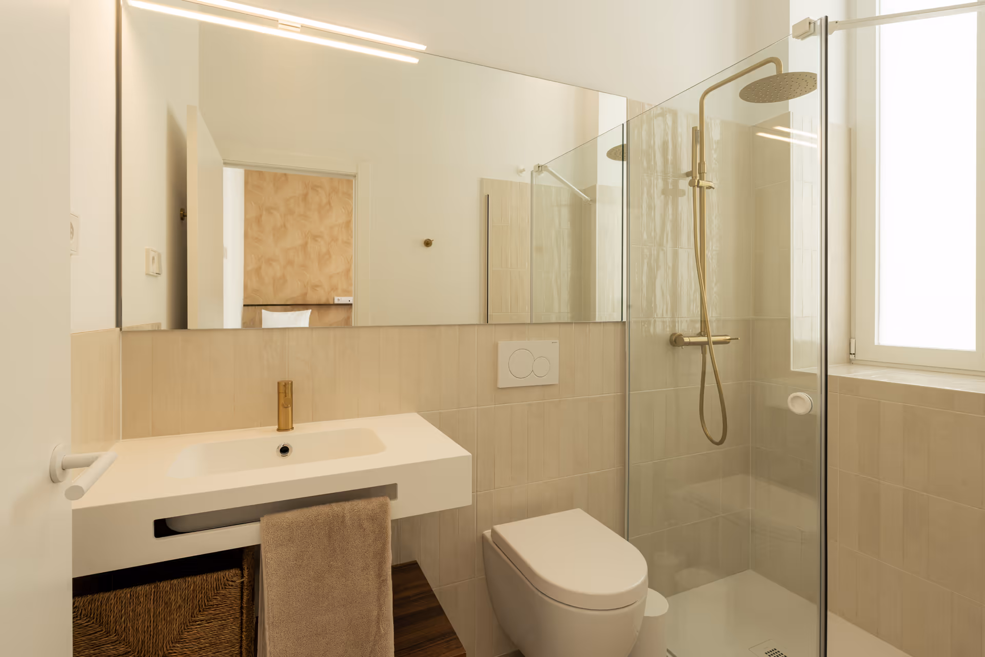 Bright bathroom in the Aurum residence with a walk-in rain shower, beige tiles, and modern brushed gold fittings