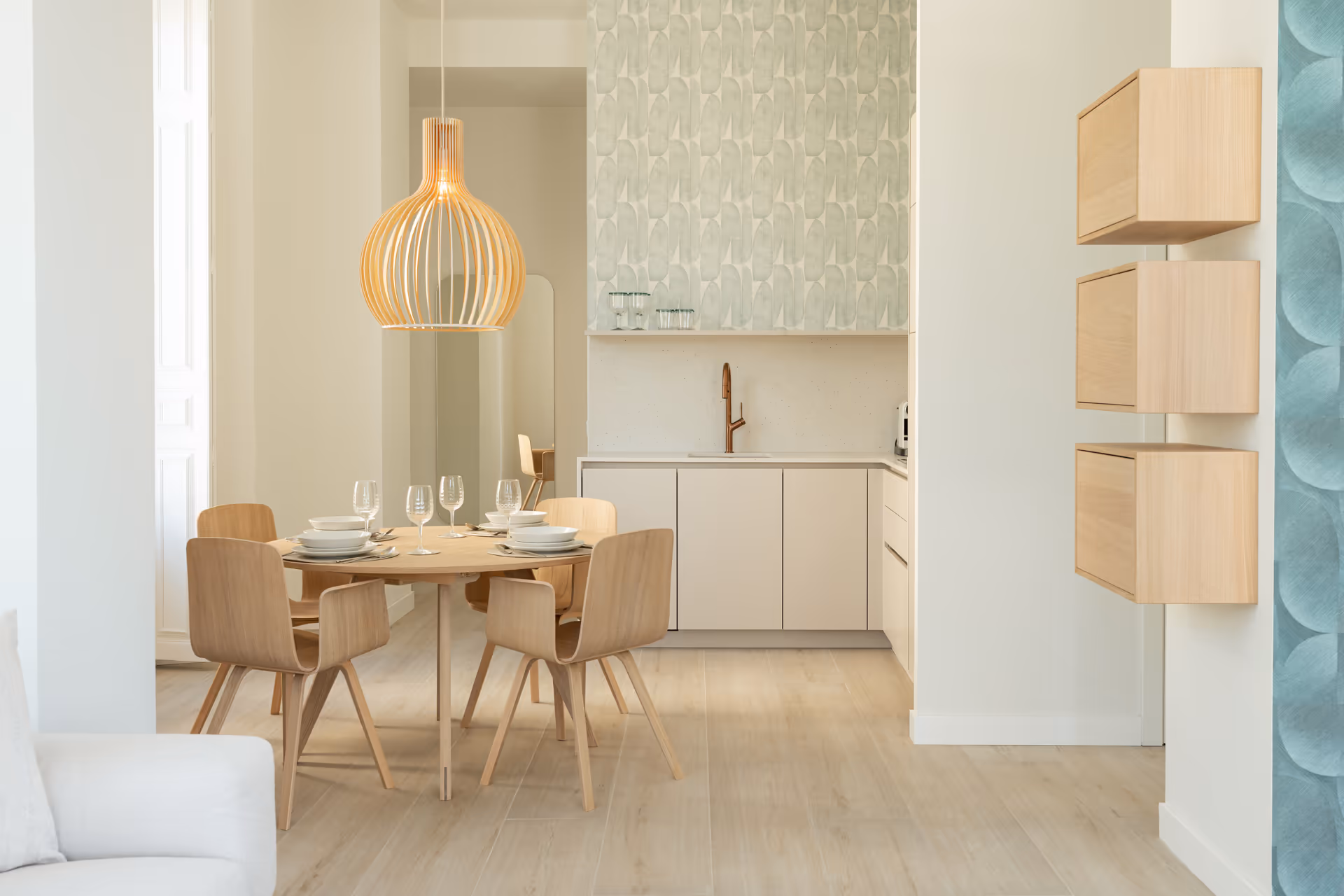 The dining area in the Azuri residence, with a round wood table, matching chairs, and a large slatted pendant lamp