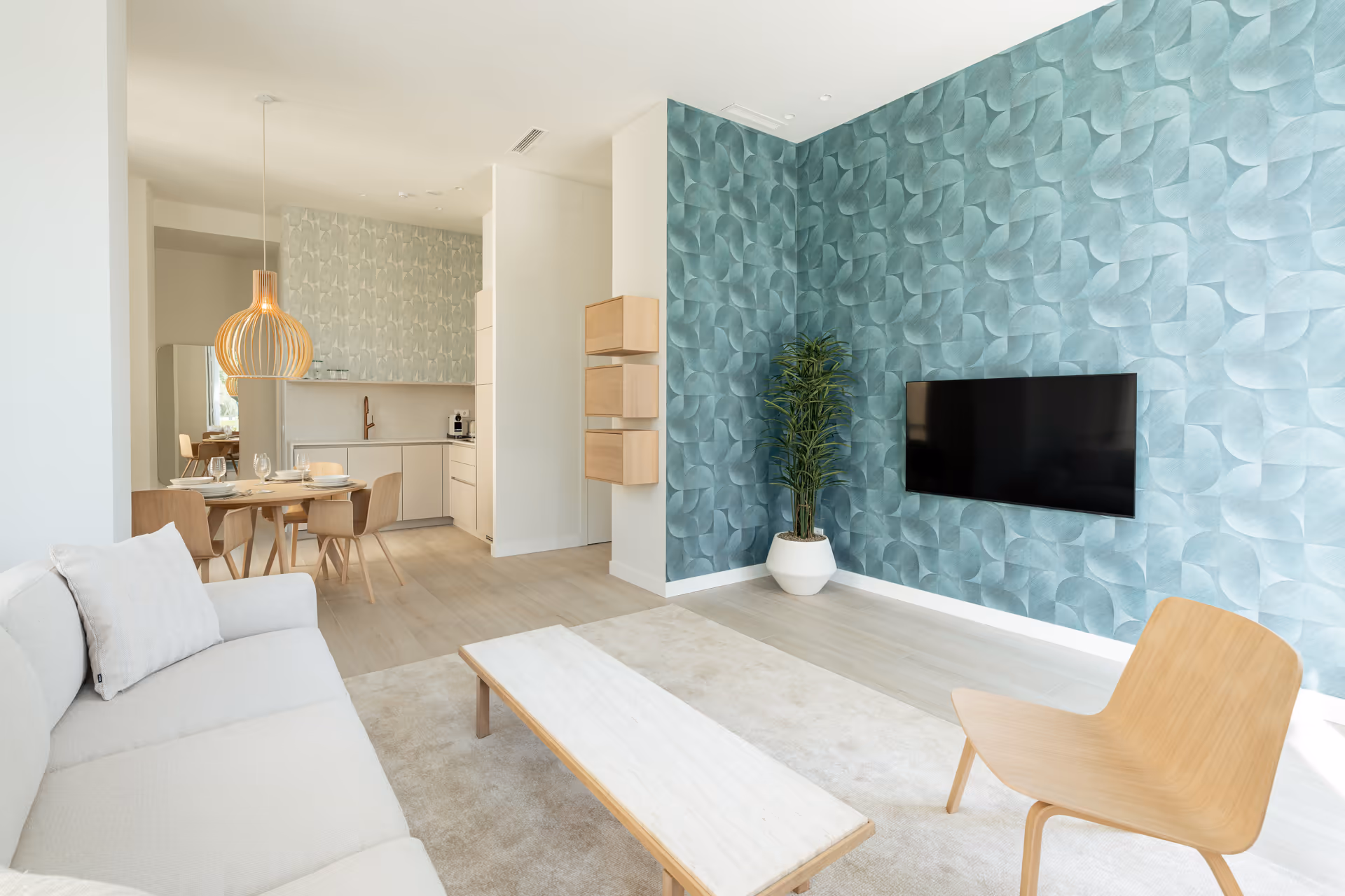 Open-plan living room in the Azuri residence with a white sofa, wooden furniture, and a teal feature wall with a TV