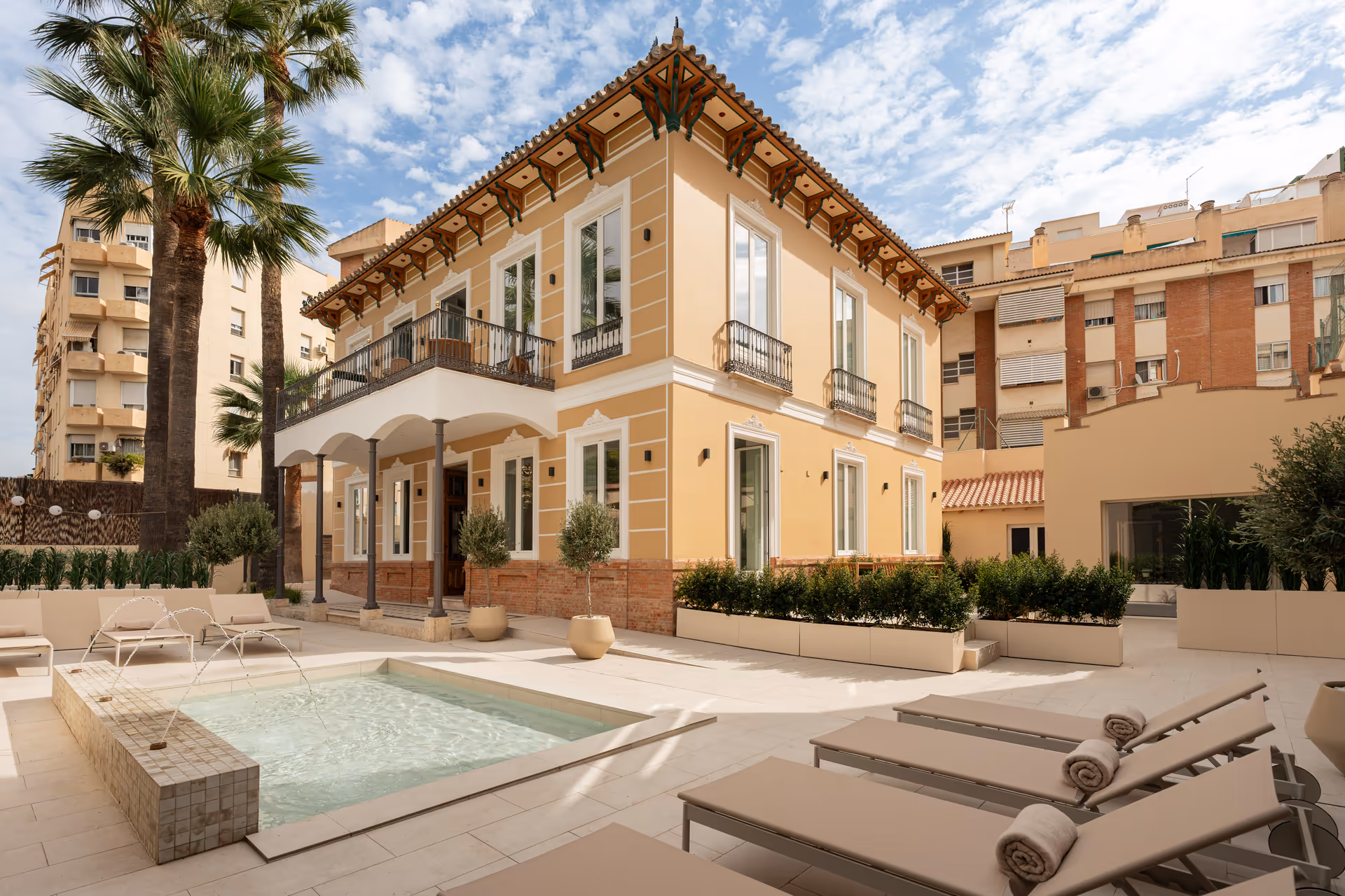 The restored yellow facade of Palacete 10, seen from the courtyard with its pond, sun loungers, and palm trees