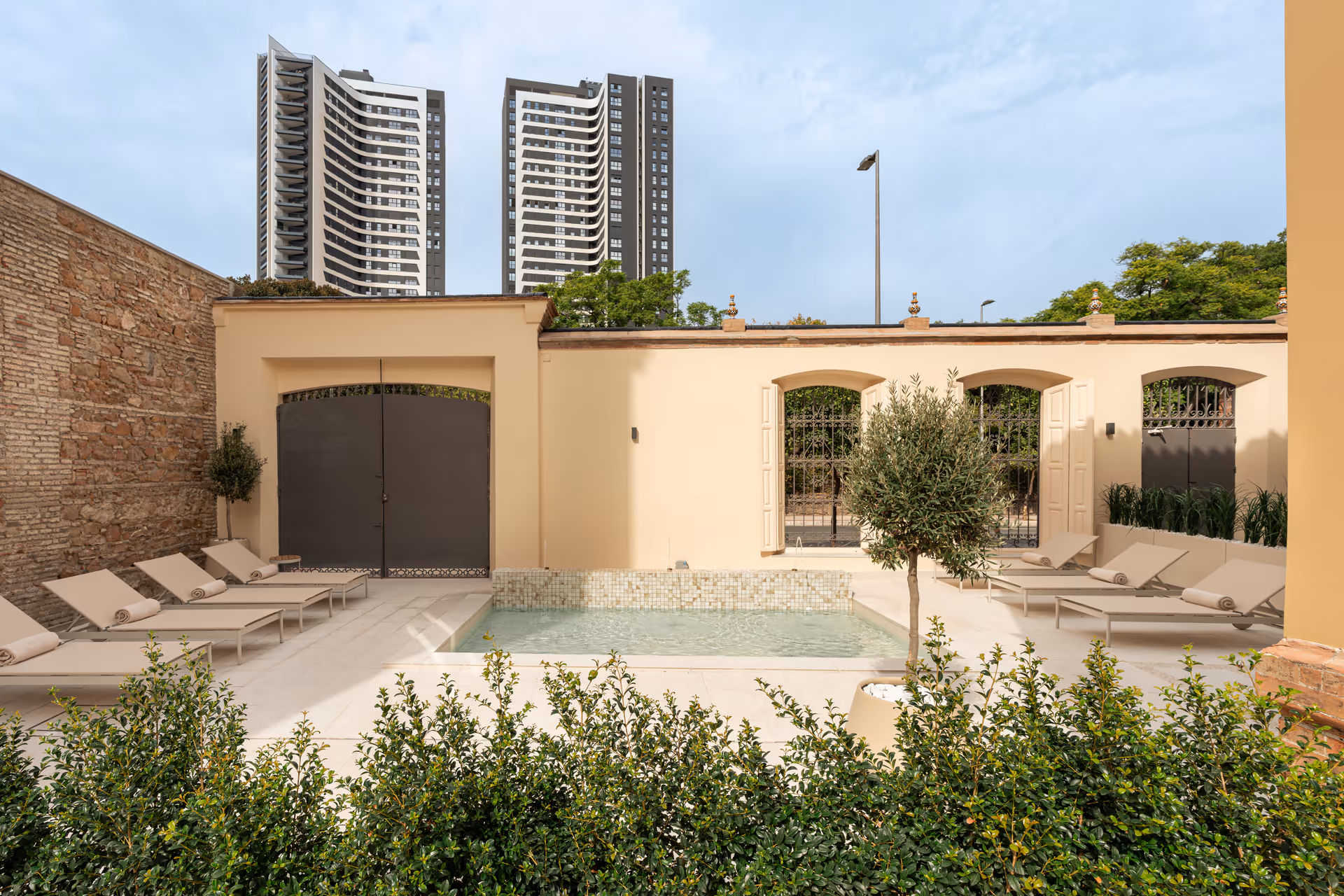 The courtyard at Palacete 10 has a tiled pond and sun loungers on a pale stone terrace, with modern towers visible behind