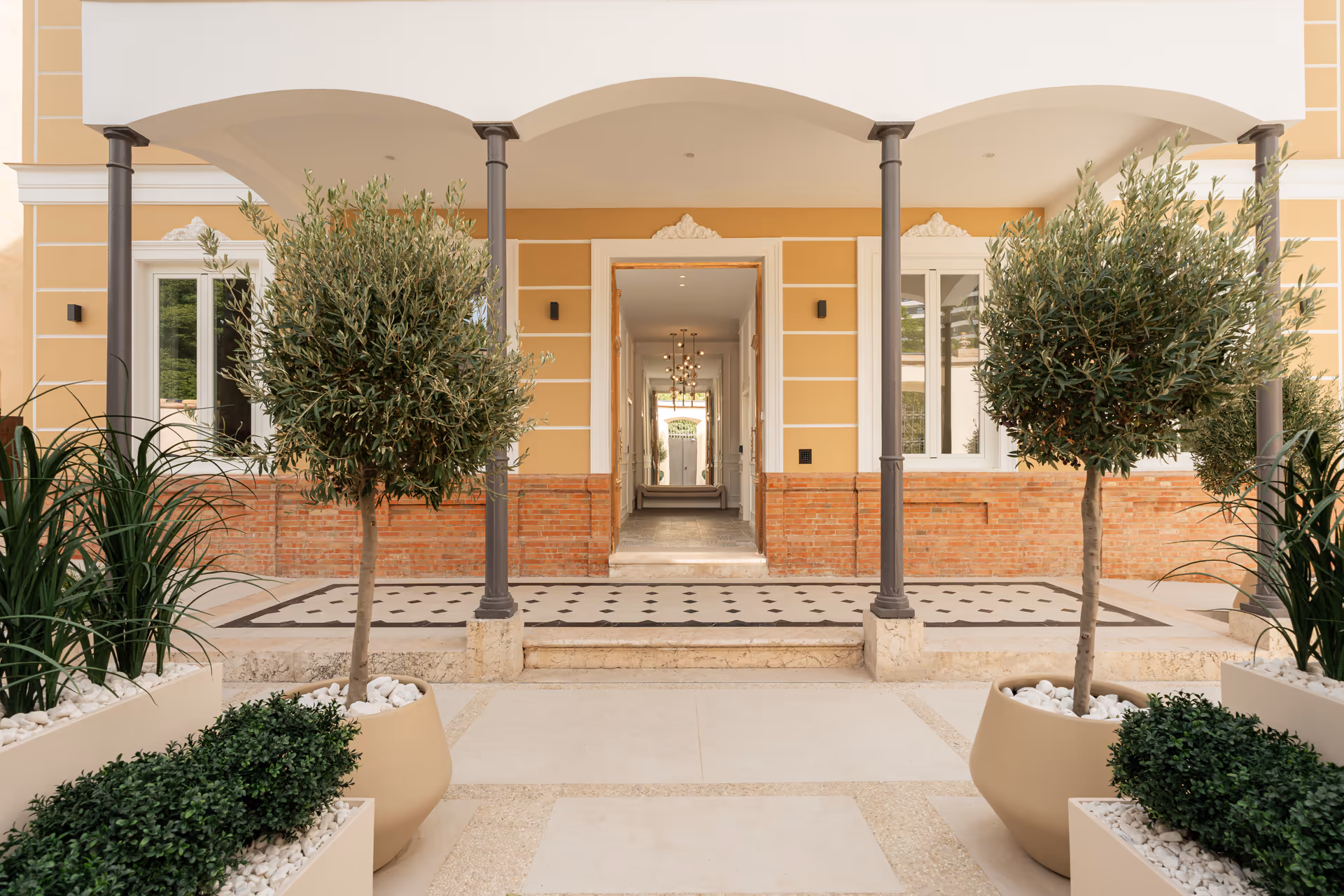 The porticoed entrance to the yellow villa, seen from the courtyard with its potted olive trees and plants