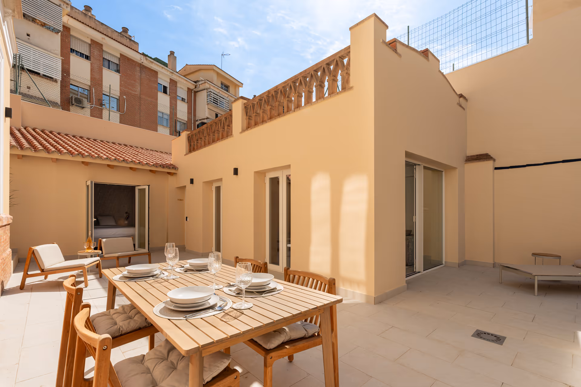 The sunny private terrace of the Toro residence, with a wooden dining table set for six and a view into the bedroom