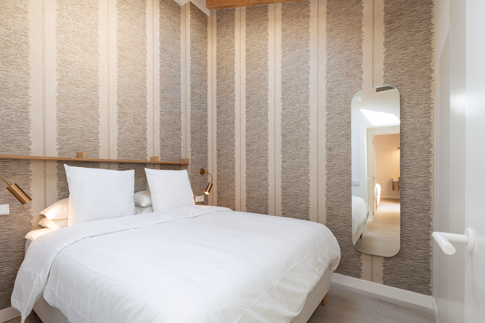 Double bed with white linen in the Toro residence bedroom, set against a wall with textured striped wallpaper and a wooden headboard shelf