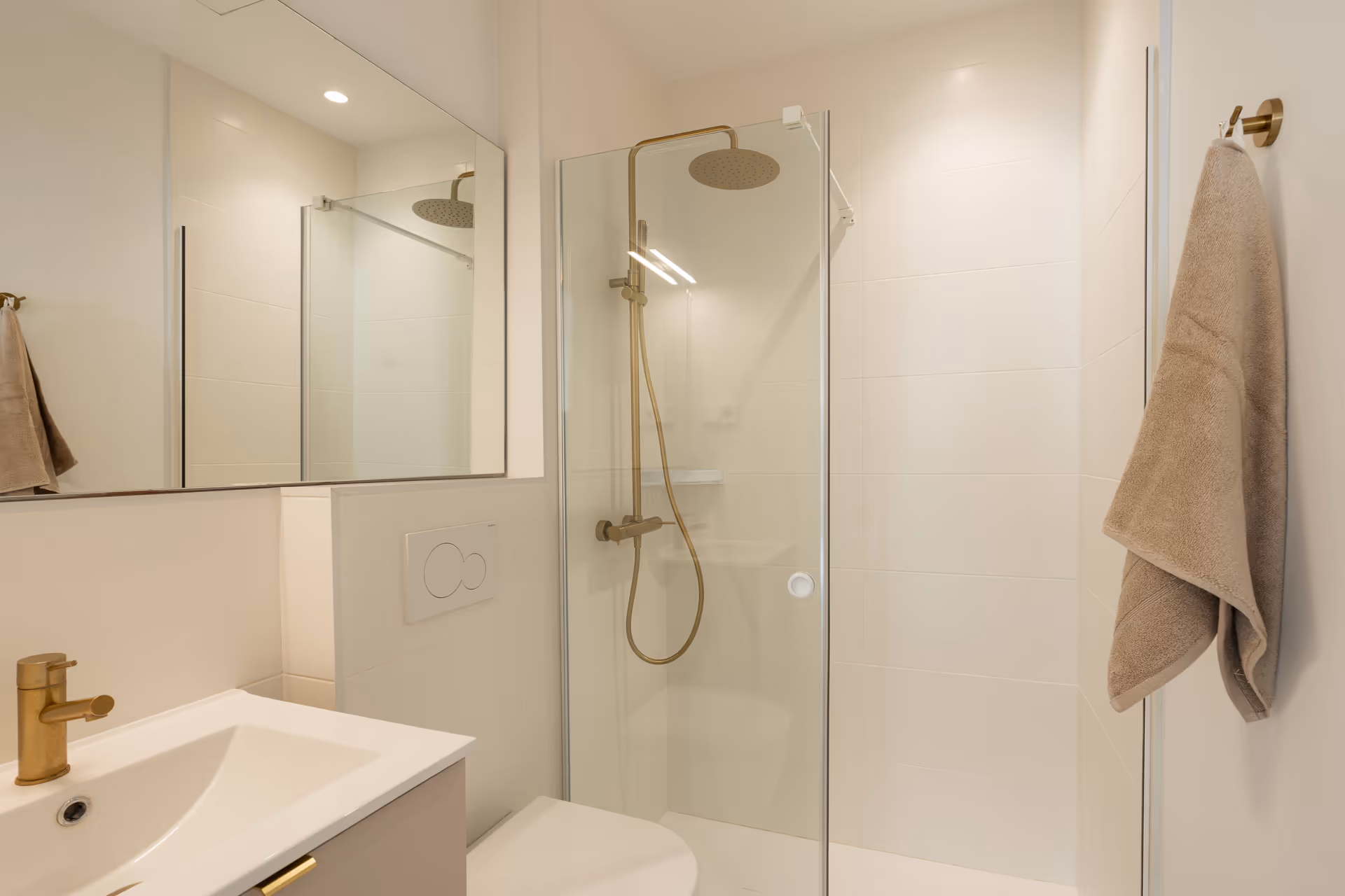The warmly lit bathroom in the Toro residence, with a walk-in rain shower, white tiles, and brushed gold fittings