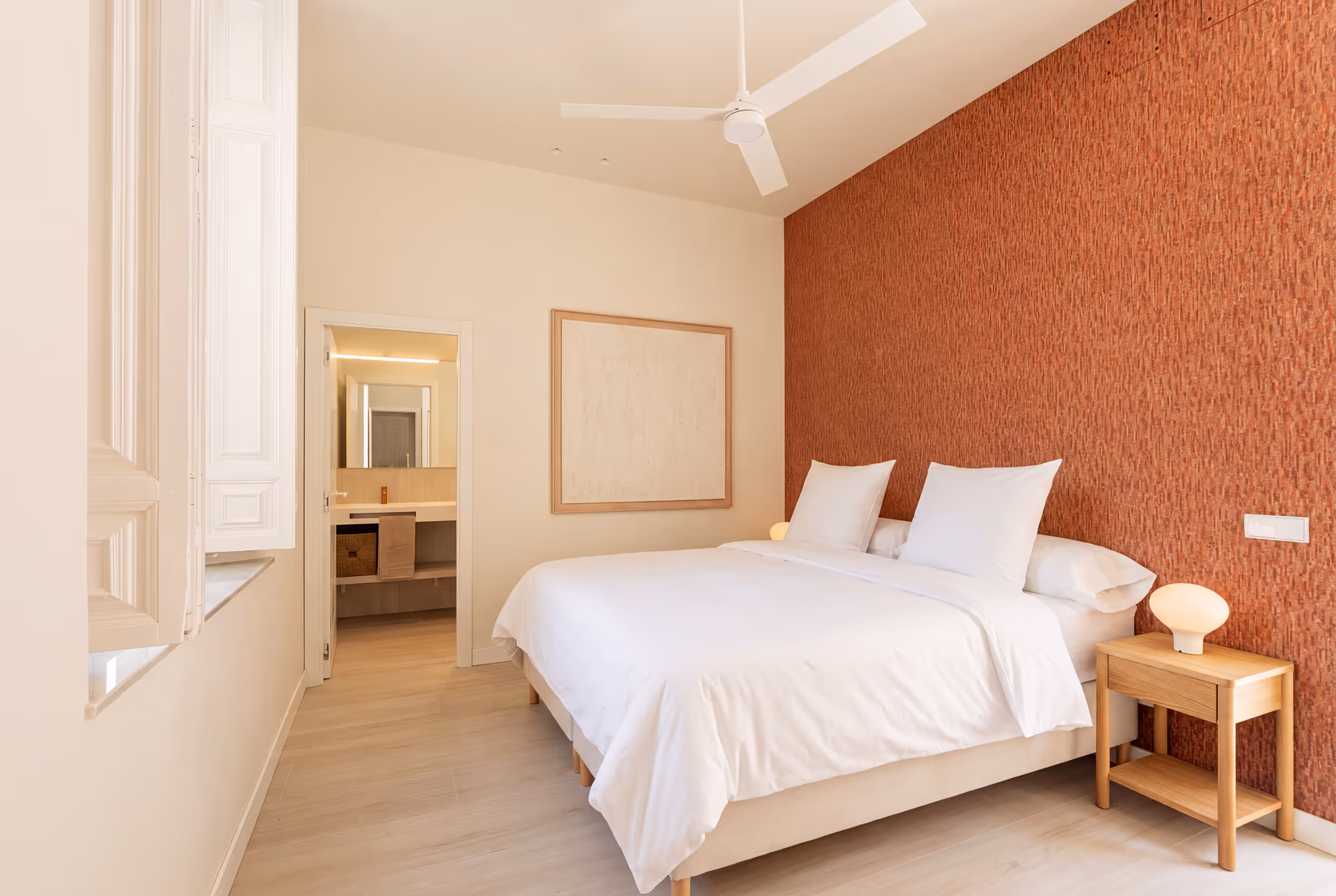 The bedroom in the Vino residence has a textured terracotta feature wall behind the double bed, with the ensuite bathroom visible