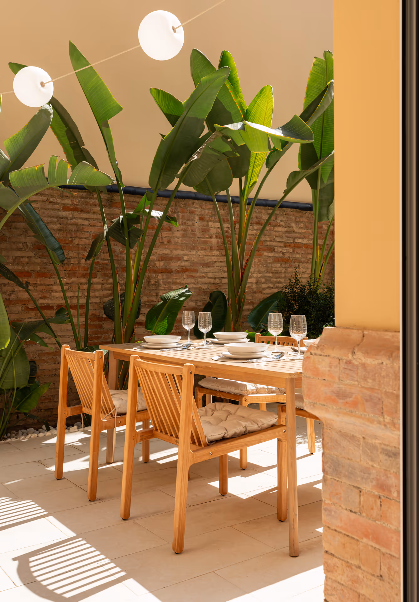 The sunny private patio of the Vino residence, with a wooden dining table set for a meal beside lush plants