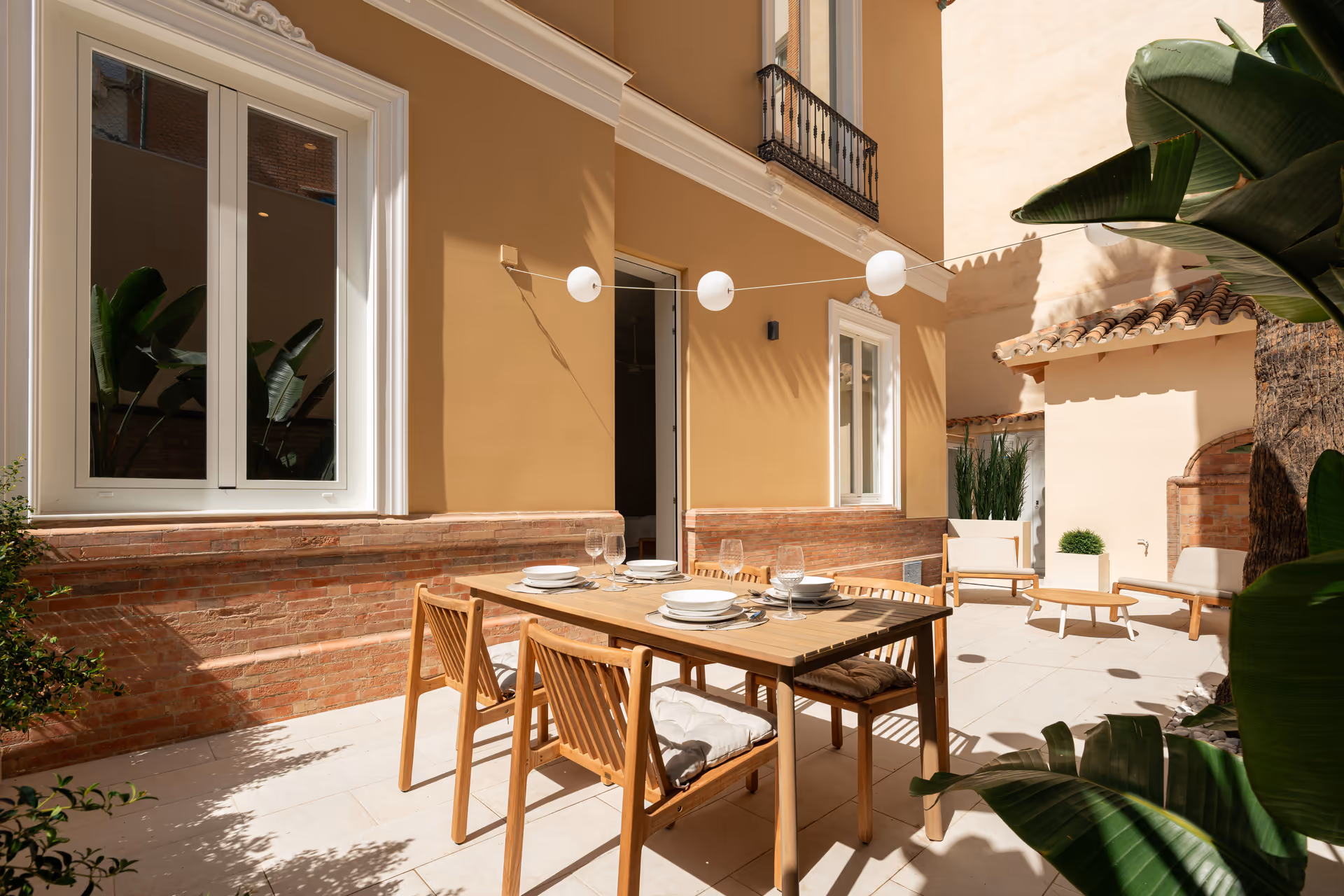 The sunny private terrace of the Vino residence, with a wooden dining table set for four against an ochre wall