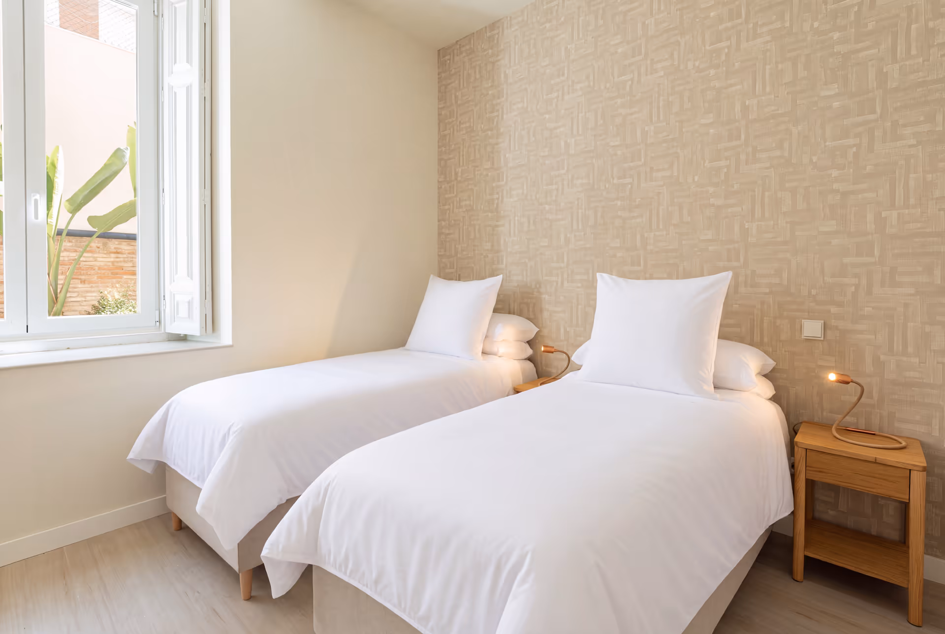The twin bedroom in the Vino residence, with two single beds, patterned wallpaper, and a window overlooking a private patio