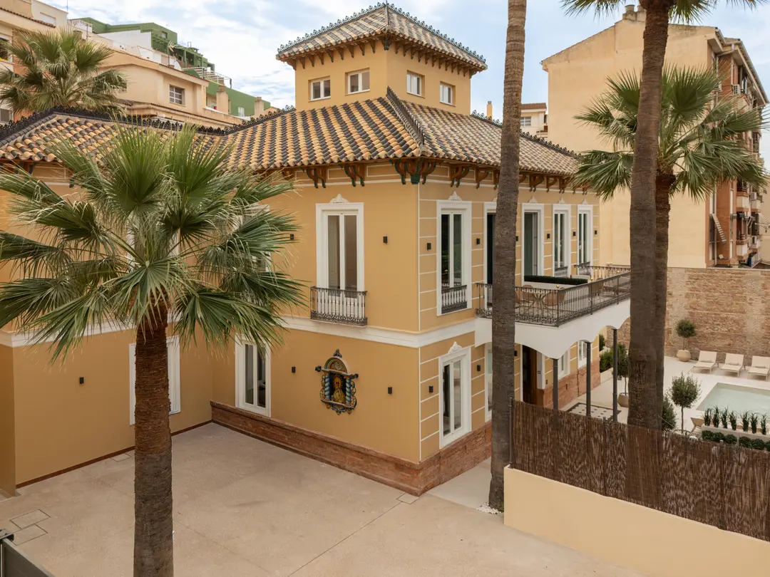 Aerial view of Palacete 10, an ochre villa with a tiled roof and tower, surrounded by palm trees and a pond