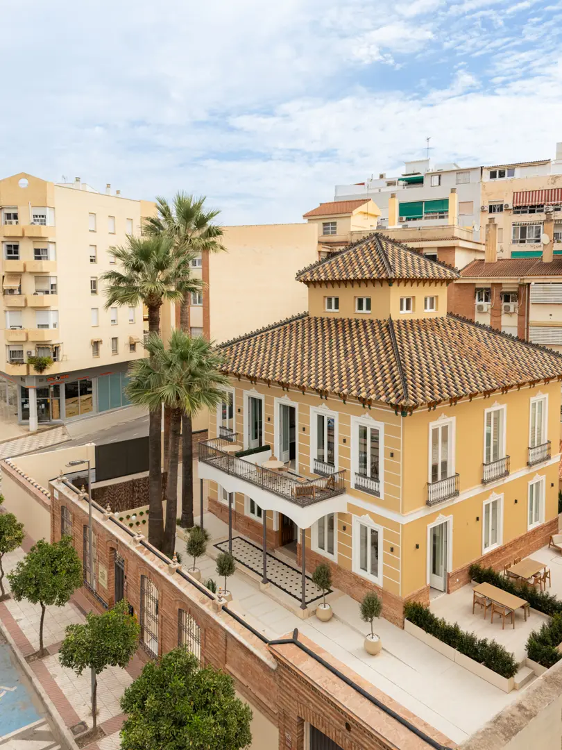 Aerial view of the restored yellow villa, Palacete 10, with its tiled roof, terraces, and surrounding palm trees in Málaga