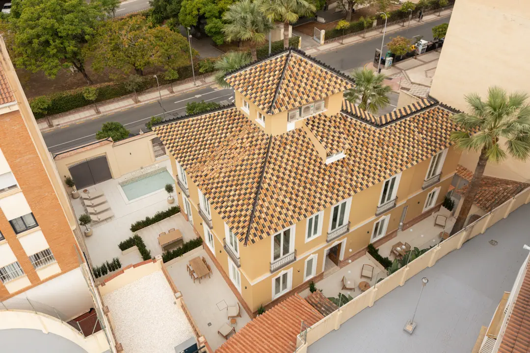 Aerial view of the restored Palacete 10 villa, showing its patterned tiled roof, yellow facade, and private courtyards with a pond
