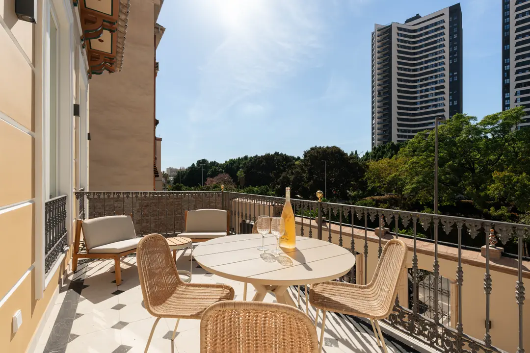 The sunny balcony of the Aurum residence, with a dining table, wicker chairs, and views over Málaga's modern architecture