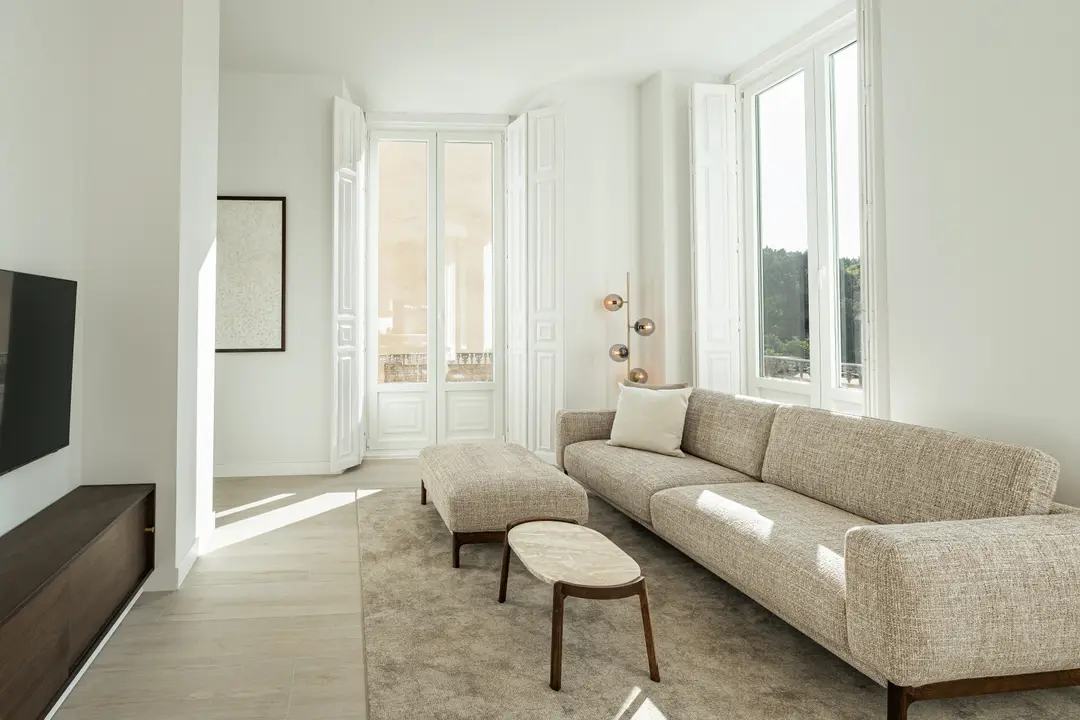 Sunlit living room in the Aurum residence, featuring a large textured sofa, marble coffee table, and tall windows with shutters