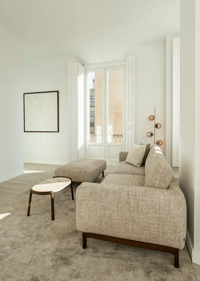 Living room in Aurum residence with a textured beige sofa and ottoman, lit by sunlight from tall French doors