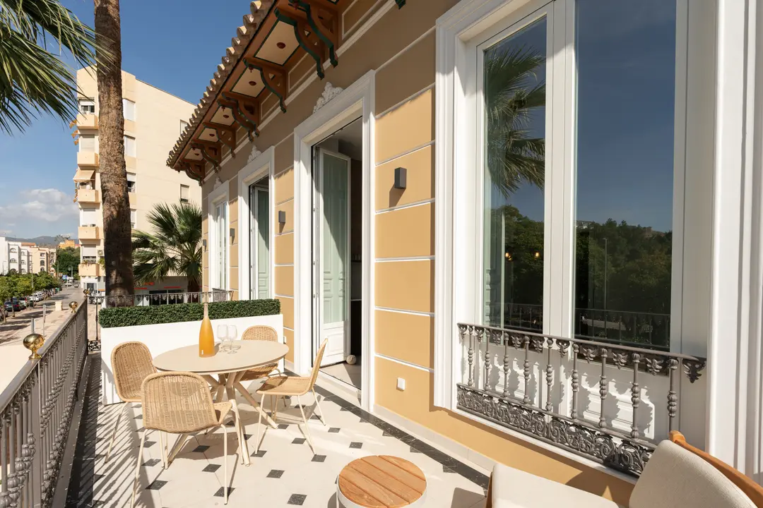 The furnished balcony of the Aurum residence, with a round dining table and wicker chairs, overlooking a tree-lined street