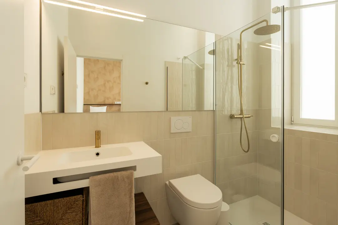 Bright bathroom in the Aurum residence with a walk-in rain shower, beige tiles, and modern brushed gold fittings