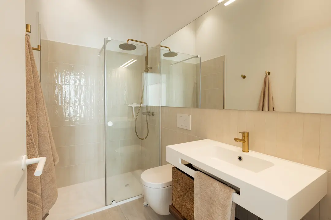 The bathroom in the Aurum residence, with a walk-in shower, white vanity unit, and brushed gold tapware and fittings