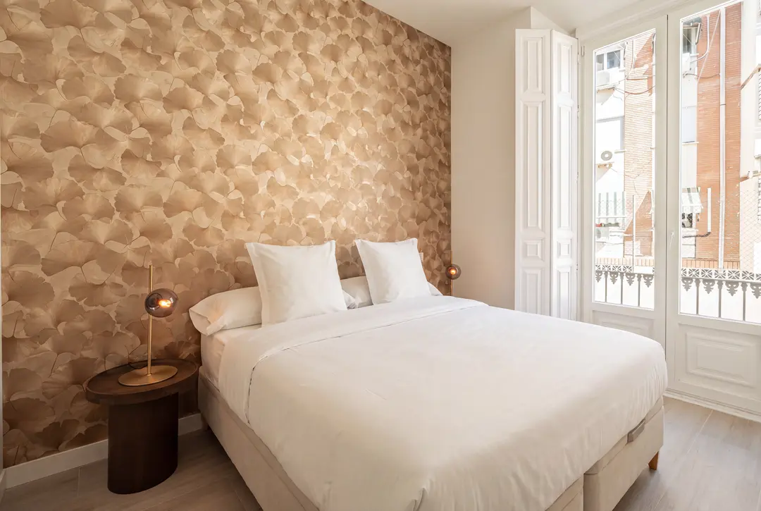 Bedroom in the Aurum residence with a double bed against a gold ginkgo-leaf feature wall and French doors opening onto a balcony