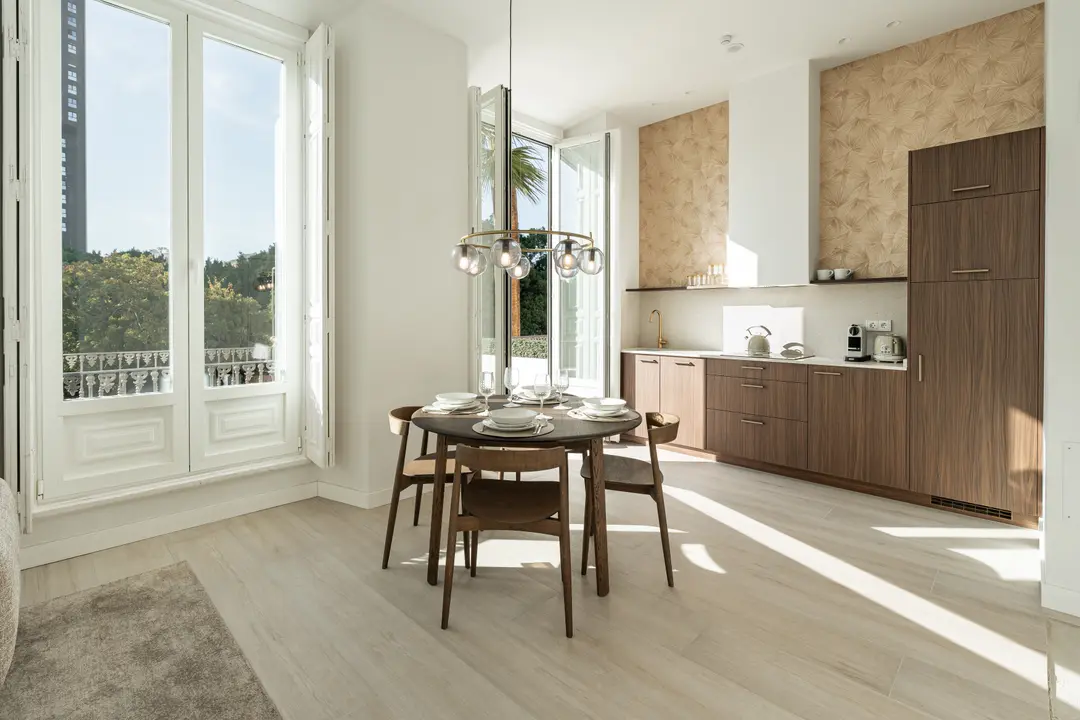 Sunlight streams into the Aurum residence's open-plan dining area and kitchen, with a round wooden table set for four