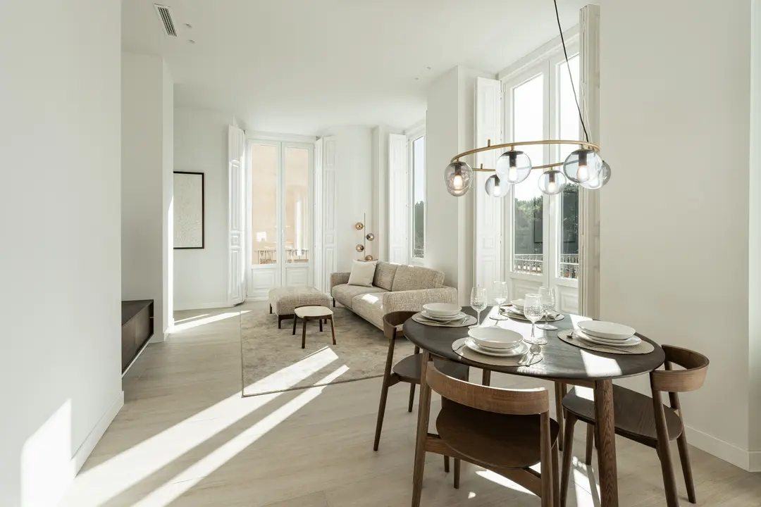 Sunlight streams into the open-plan living and dining area of the Aurum residence, highlighting the light wood floors and modern furniture