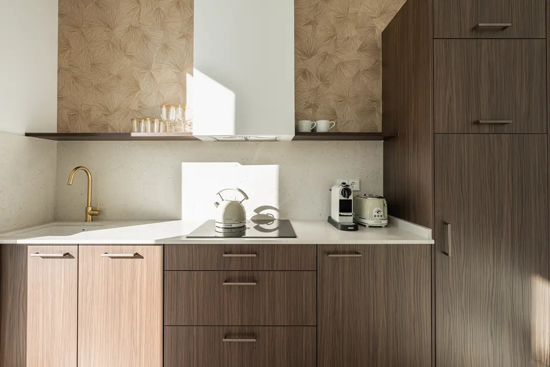 Sunlit kitchen in the Aurum residence with dark wood cabinets, a white countertop, gold tap, and patterned wallpaper