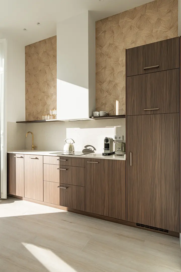 The modern kitchen in the Aurum residence, with dark wood cabinets, a brass tap, and gold fan-patterned wallpaper catching the sunlight