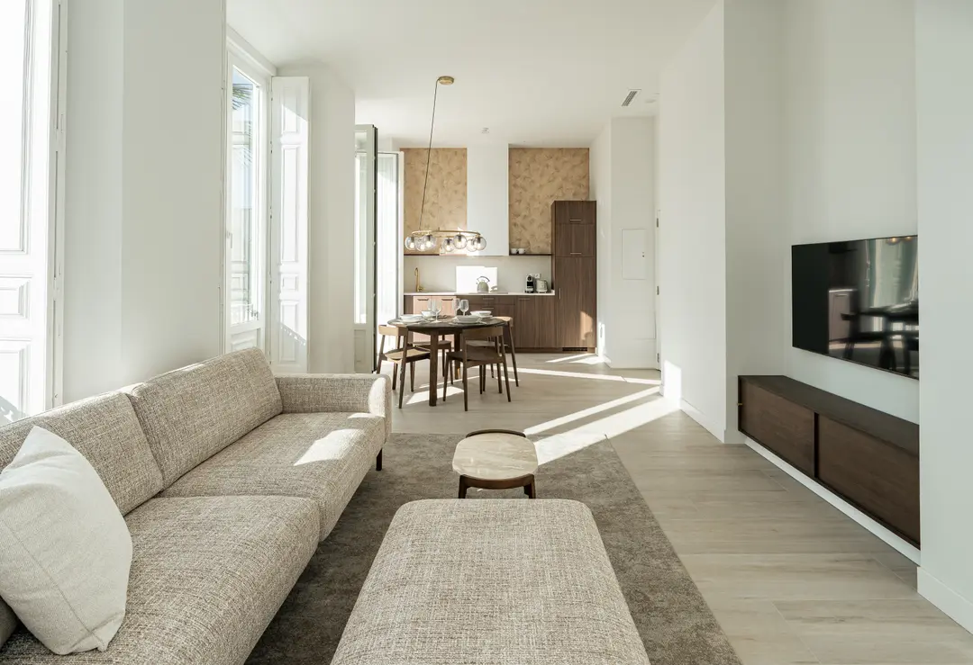 The sunlit open-plan living area of the Aurum residence, with a textured sofa, dining table, and modern kitchen