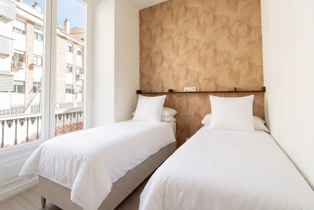 The twin bedroom in the Aurum residence, with a textured wood feature wall and a balcony overlooking a Málaga street