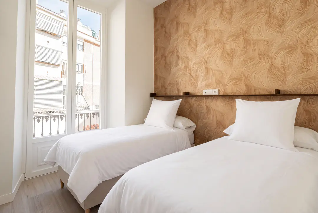 The twin bedroom in the Aurum residence, featuring textured gold wallpaper, two single beds, and a door to a balcony