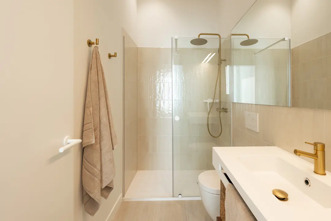 Bathroom in the Aurum residence with a walk-in shower, white vanity unit, beige tiles, and brushed gold fittings