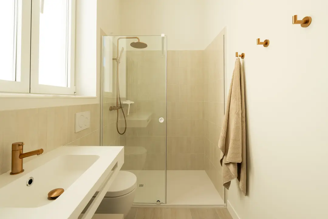 The bathroom in the Azuri residence, with a walk-in rain shower, white vanity unit, and brushed bronze fittings