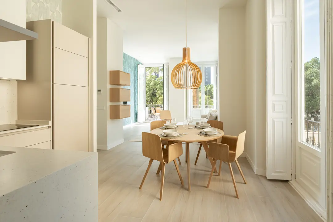 The bright dining area in the Azuri residence, with a round wooden table and a view to the living room and balcony