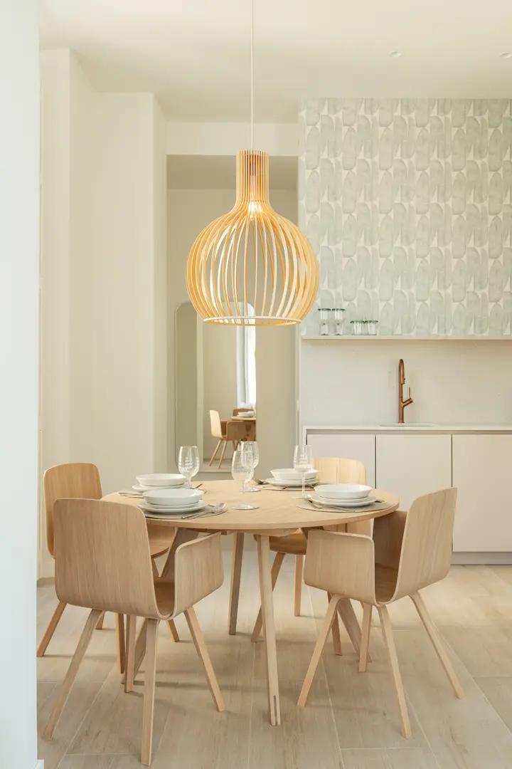 The dining area in the Azuri residence, with a round wooden table and chairs under a large slatted pendant lamp