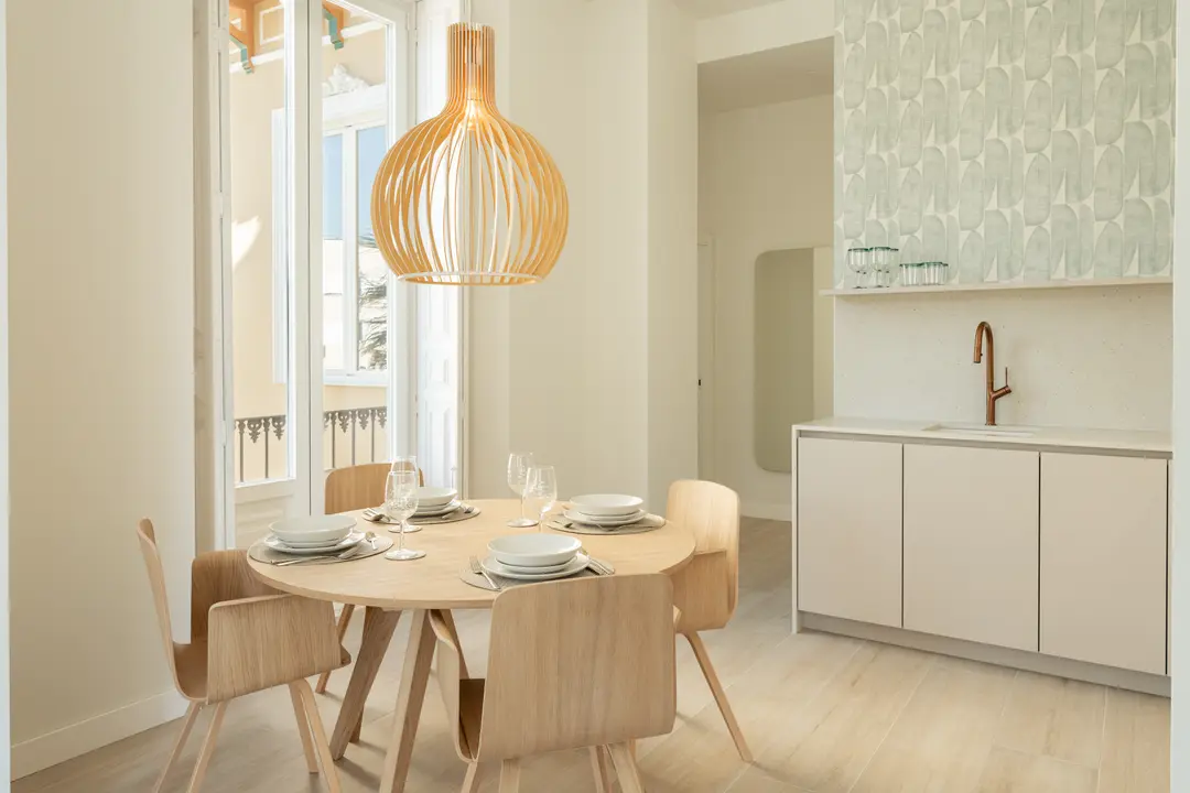 Dining area in the Azuri residence with a round oak table set for five under a large wooden pendant lamp