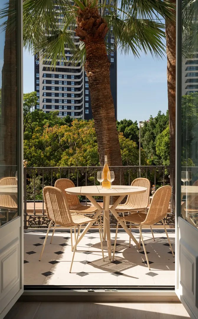 The sunny balcony of the Azuri residence, with a round table, wicker chairs, and views over the palm trees of Málaga