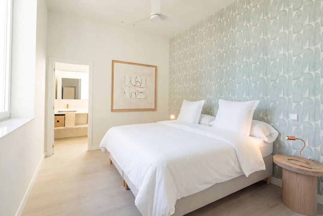 Bedroom in the Azuri residence with a double bed, textured white bedspread, and pale green patterned wallpaper behind the headboard