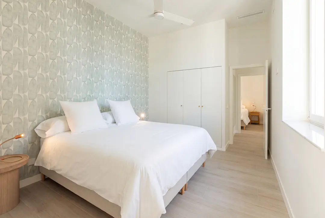 A double bedroom in the Azuri residence with a pale green patterned feature wall and light wood flooring, looking towards another bedroom