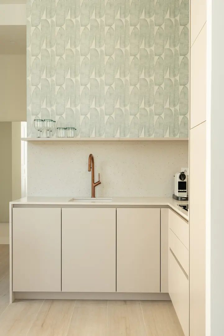 Detail of the Azuri residence kitchen, showing cream cabinets, a copper tap, and a wall with green patterned wallpaper