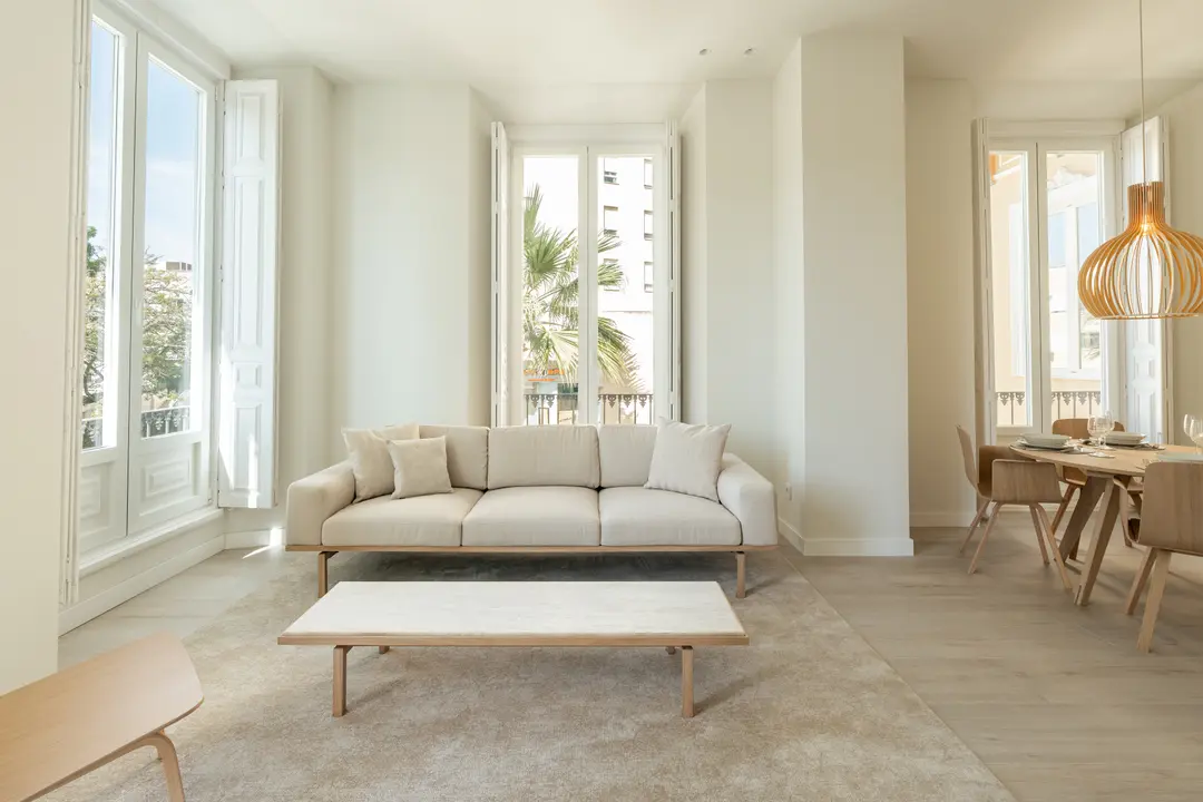 Bright living and dining area in the Azuri residence with a light sofa, wooden furniture, and tall open windows