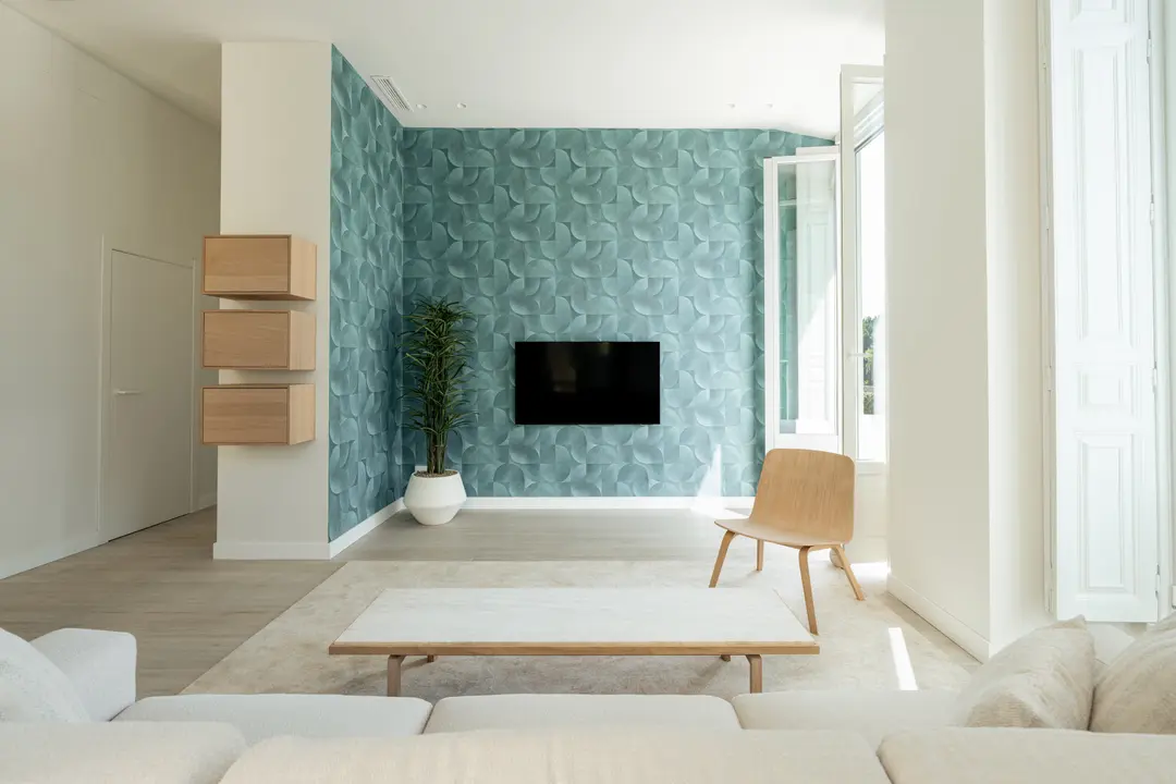 Bright living room in the Azuri residence with a textured blue accent wall, marble coffee table, and light wood furniture