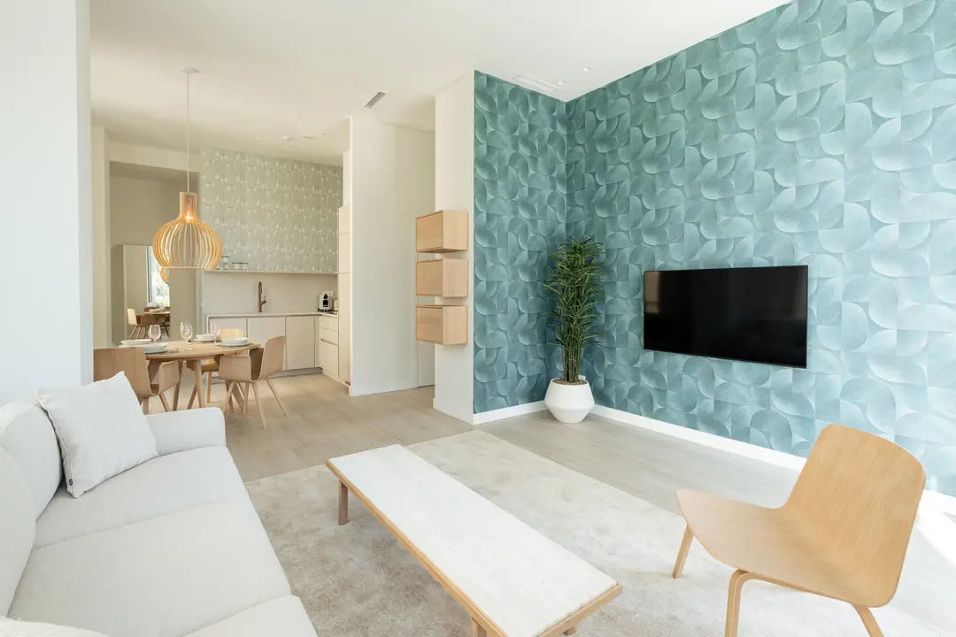 Open-plan living room in the Azuri residence with a white sofa, wooden furniture, and a teal feature wall with a TV